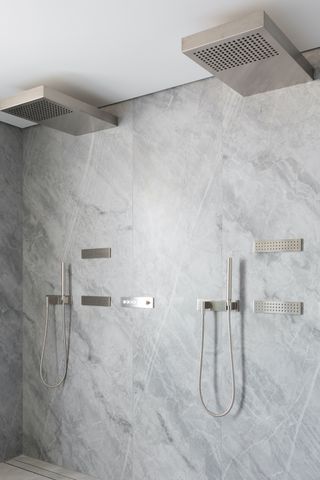 Shower design for a small bathroom illustrated by square chrome shower fittings in a marble shower room.