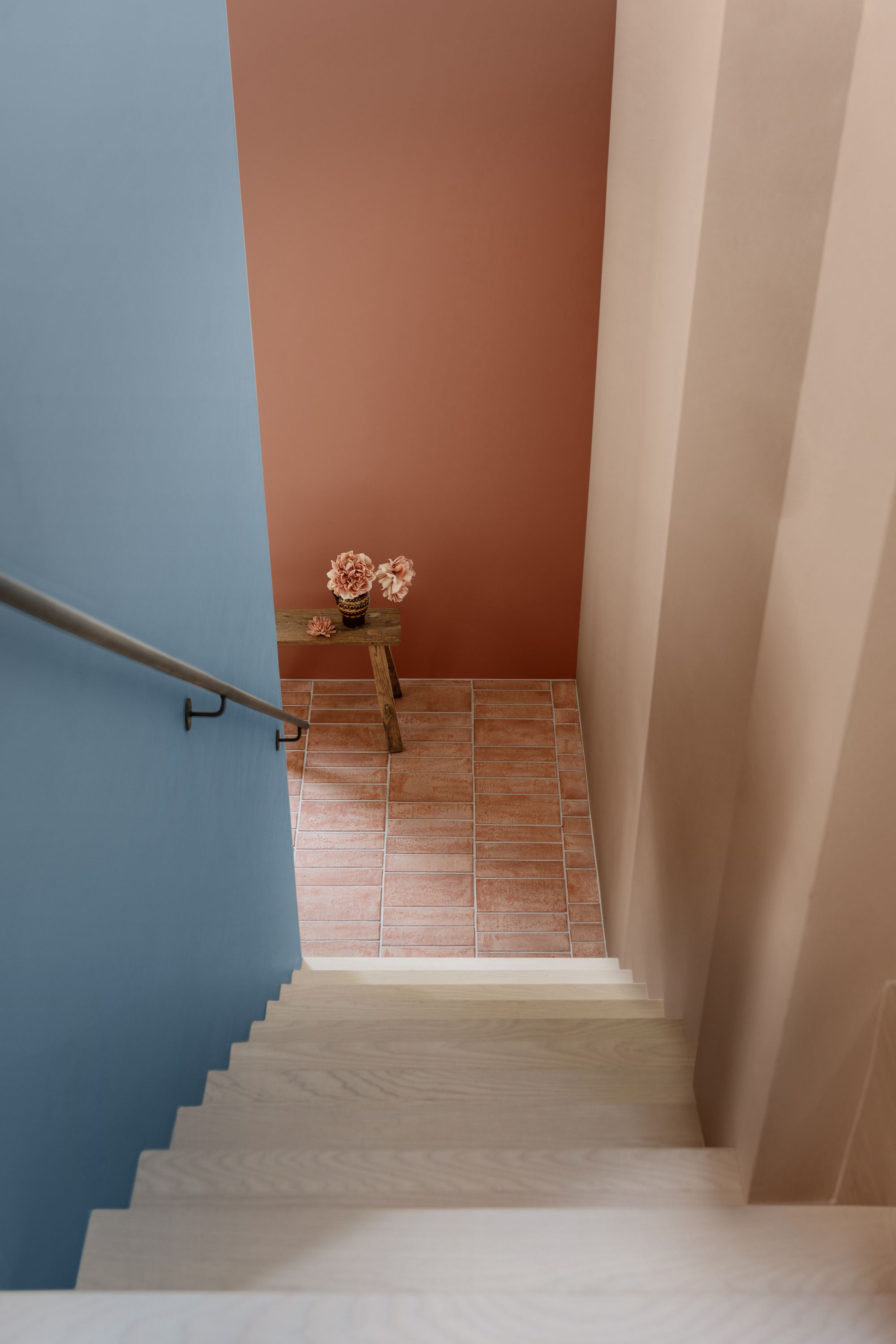 A staircase with one wall that is blush pink/beige and one that is light blue. The wall at the bottom of the stairs is terracotta. 