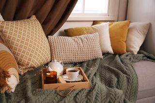 Cosy lounge area with a sage green knitted blanket and yellow, cream and white cushions.