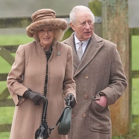 Queen Camilla wearing a tan coat and hat standing with King Charles outside church