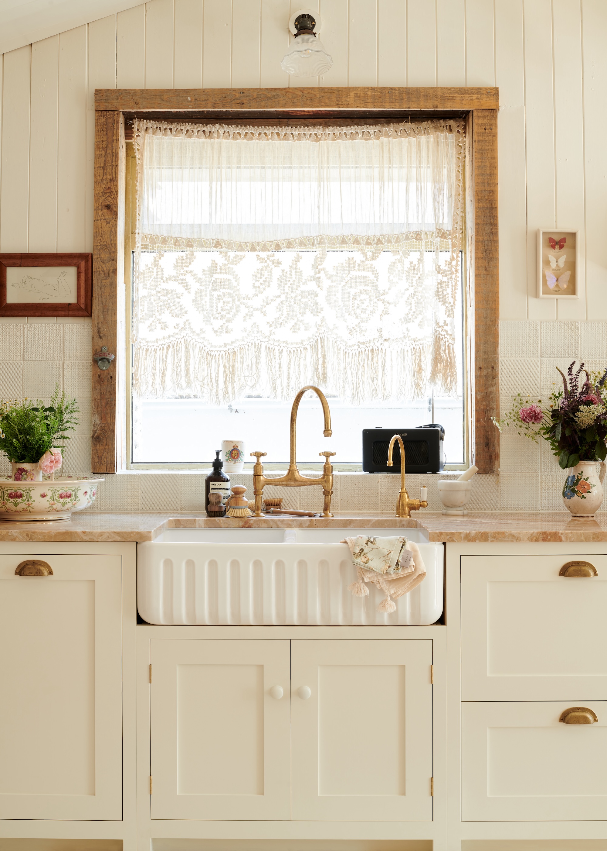 a vintage style kitchen showing cream cabinets, a large Belfast sink and aged brass kitchen taps