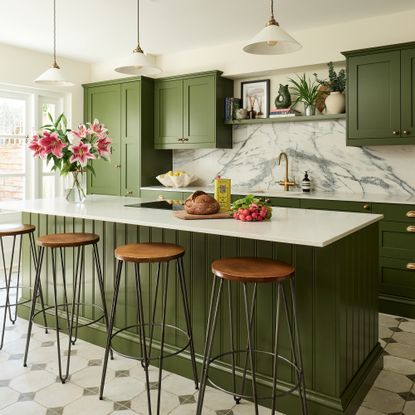 small green kitchen with a run of cabinetry quartz worktop and marble splashback and island with bar stools 