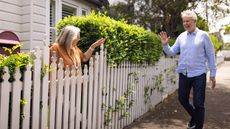 A woman in her yard waves to a neighbor walking by.
