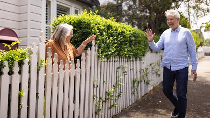 A woman in her yard waves to a neighbor walking by.