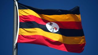 The flag of Uganda flying against a clear blue sky