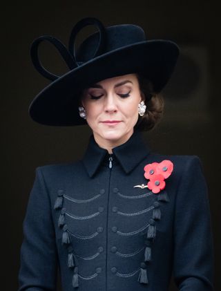 Kate Middleton wearing a black coat and hat and closing her eyes at Remembrance Day ceremony