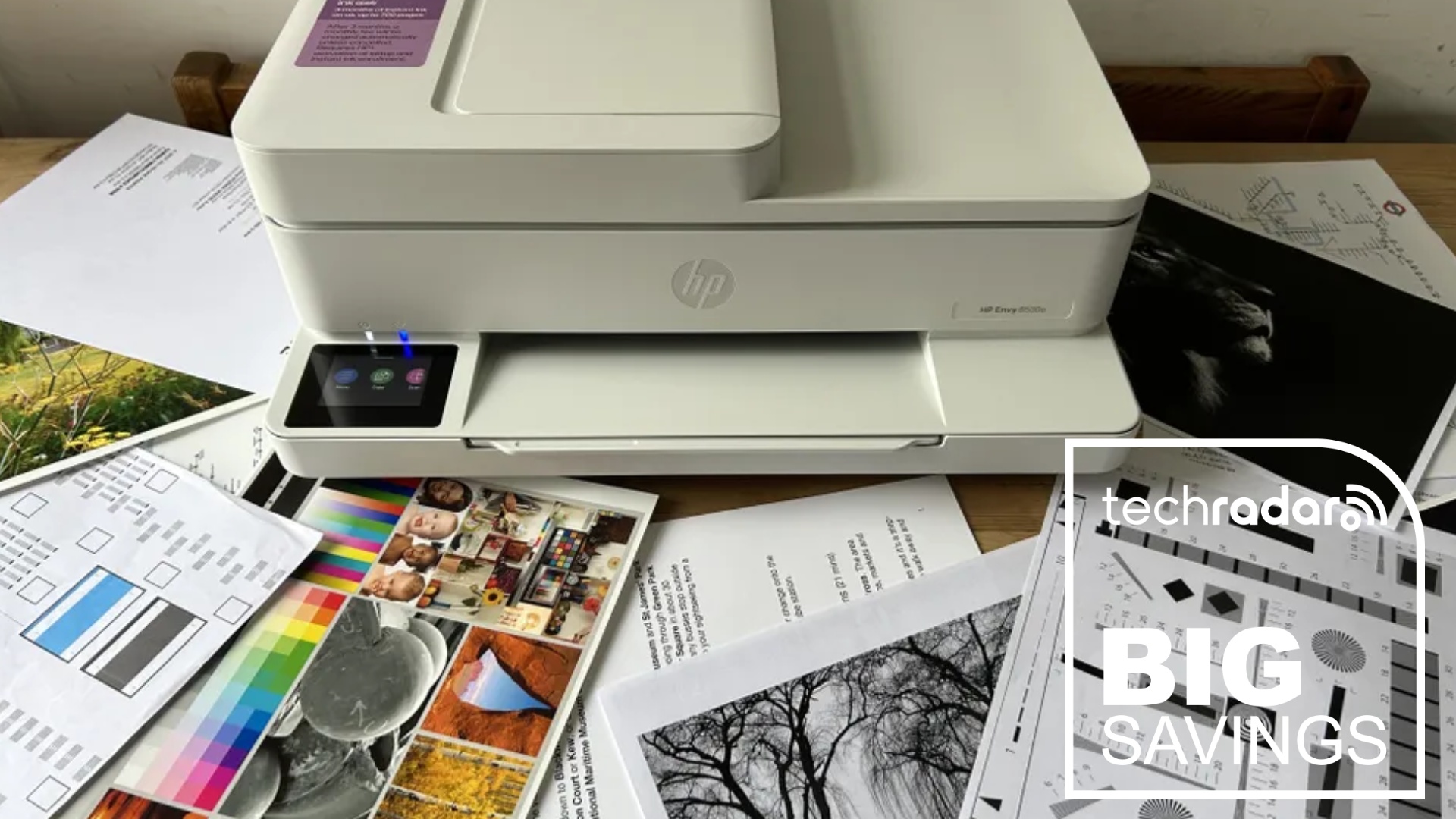 The HP Envy 6555e during our review surrounded by print-outs, next to a TechRadar badge that reads 'Big Savings'
