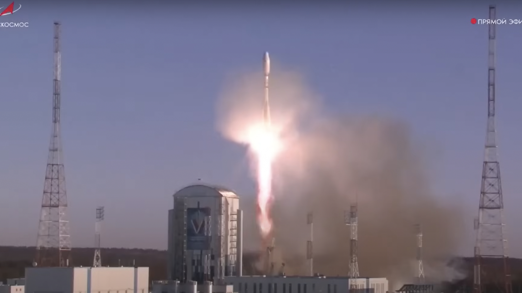 A rocket blasts off near launch facilities and tall lightning towers.