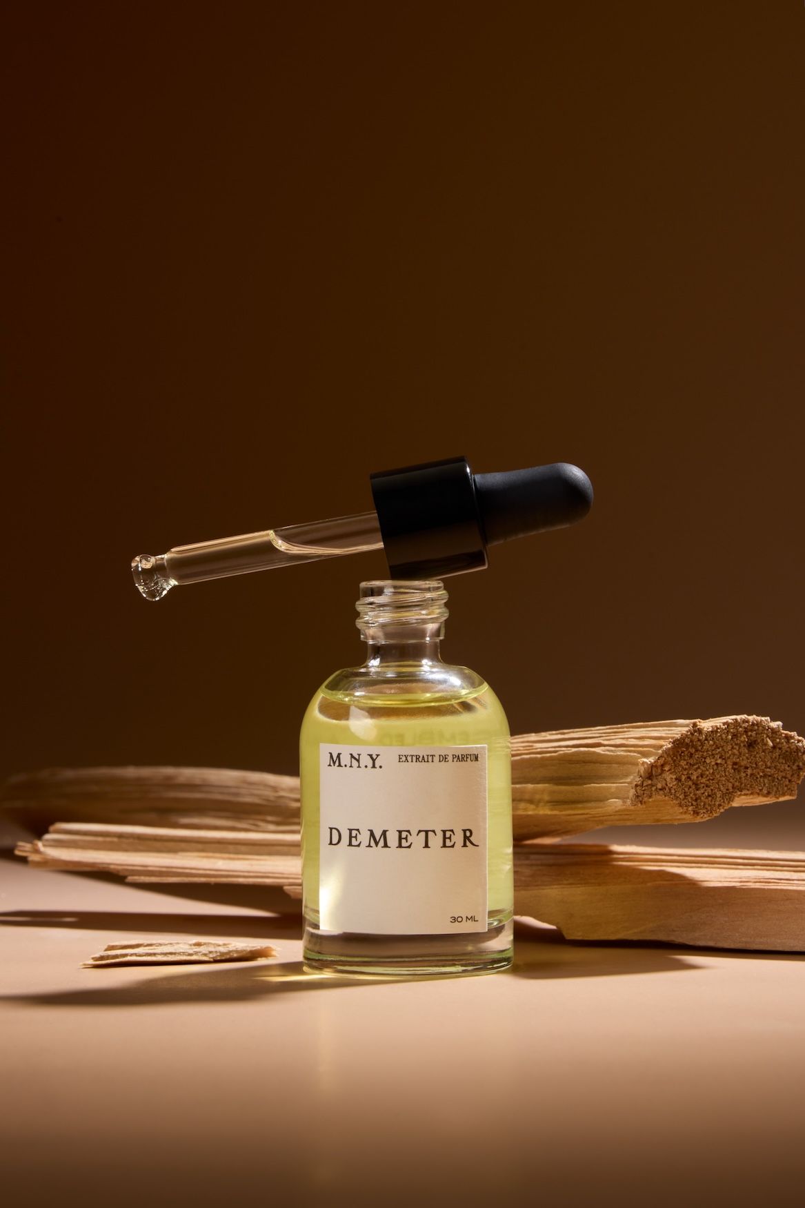 A vile of fragrance oil with the word "Demeter" on the label, set in front of pieces of wood.