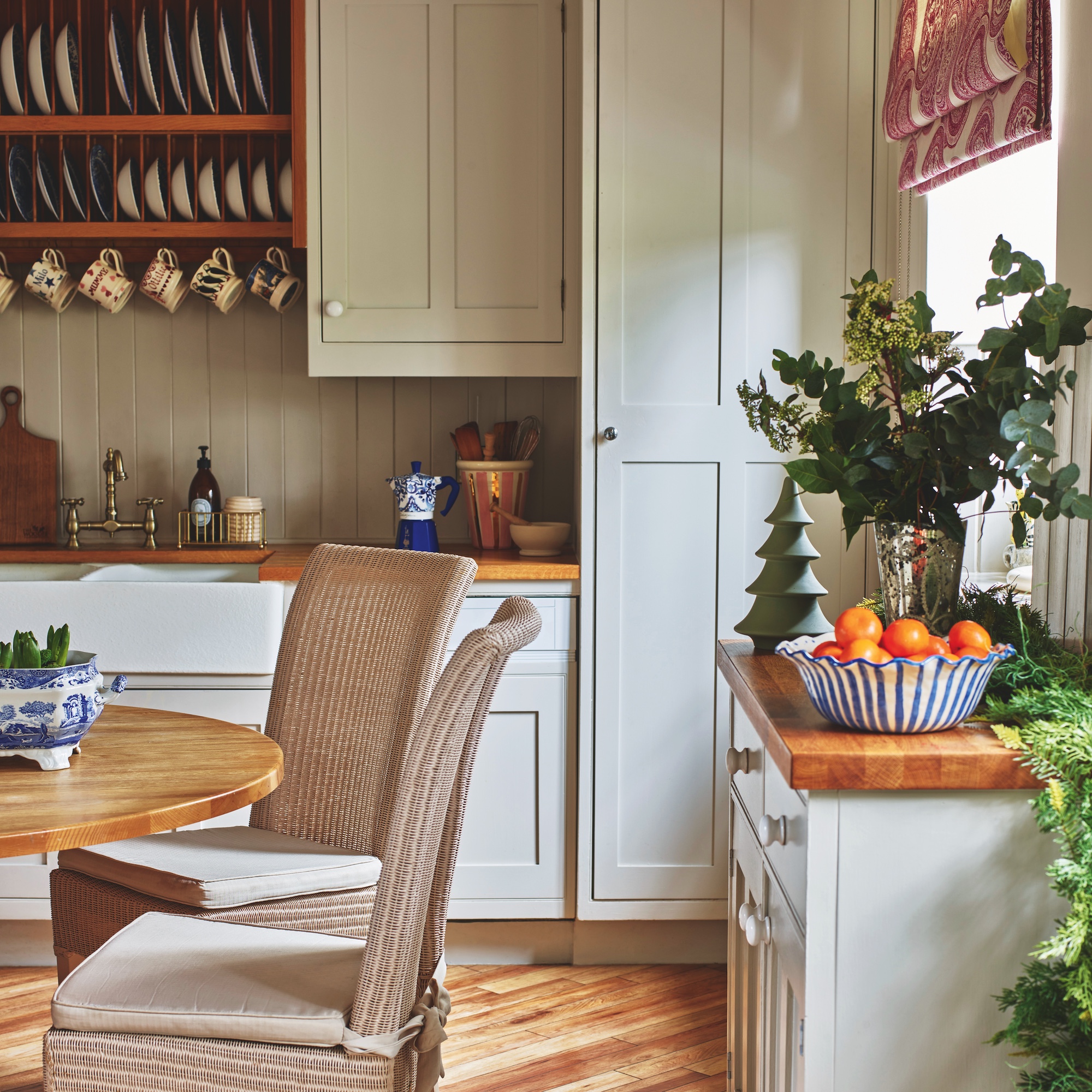 farmhouse style kitchen with white painted wooden units and dresser plate rack, with circular wooden dining table and wicker chairs