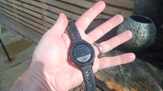 En hand som håller i en svart Garmin Forerunner 255S Music utomhus på en veranda.