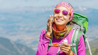 Hiker woman applying sun cream to protect her skin from dangerous uv sun rays high in mountains