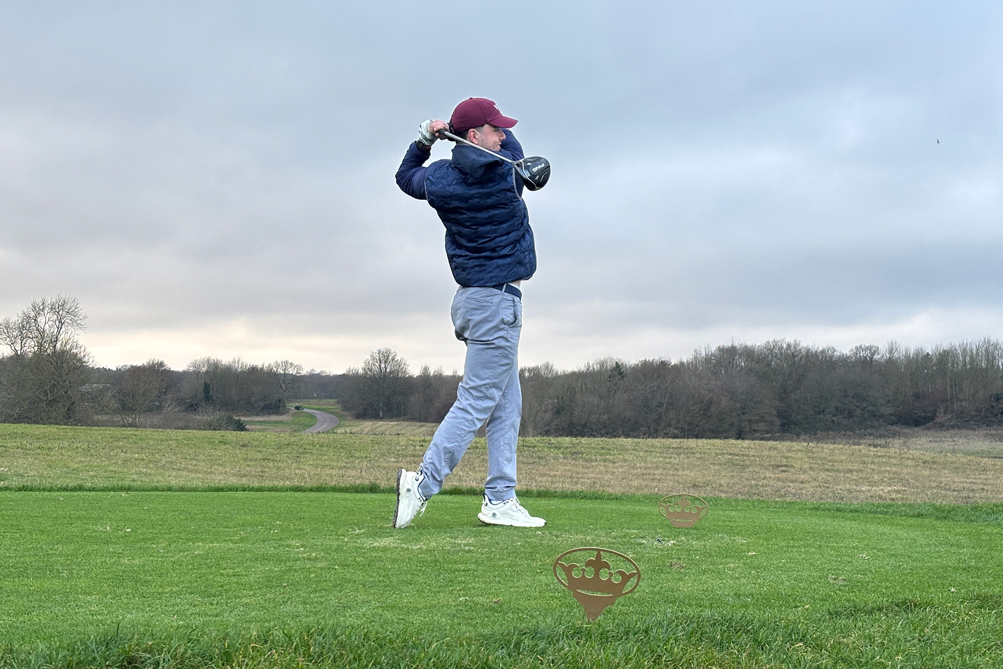 Conor Keenan hitting a tee shot at the London Club, with the gold London Club tee markers on the ground