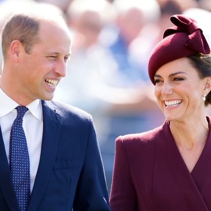 Kate Middleton wears a dark red coat and matching hat and Prince William wears a navy suit and matching blue tie