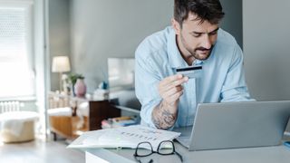 A man sitting in front of a laptop and holding a credit card