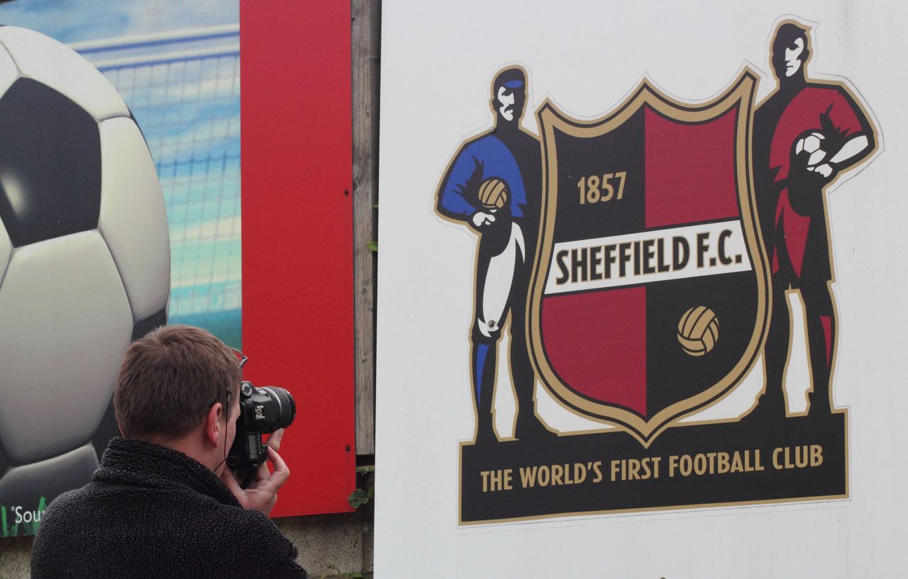 A man photographs a sign featuring the club crest of Sheffield FC, the oldest football club in the world