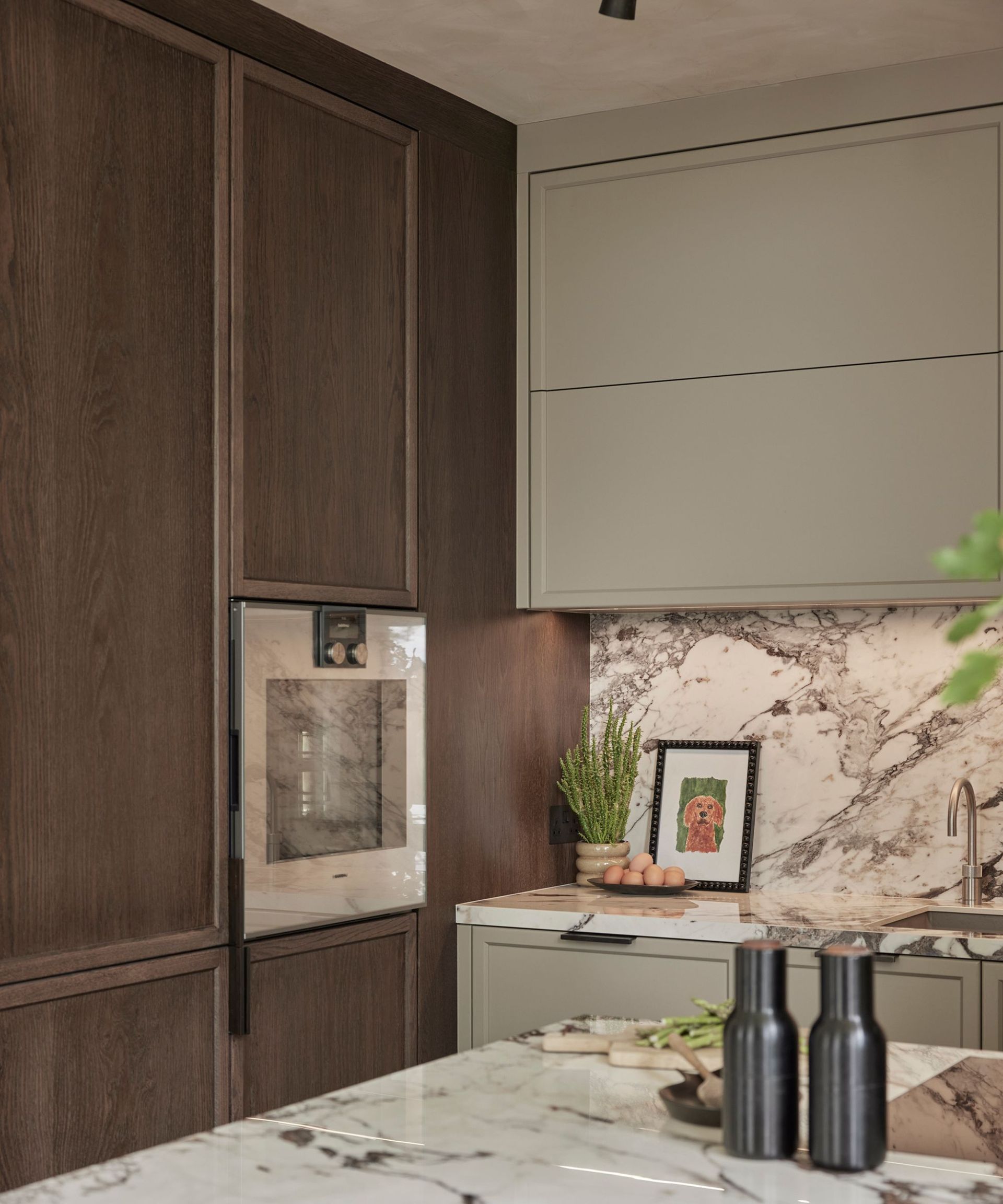 A kitchen with wooden full length cabinets, gray upper cabinets, and a marble countertop and backsplash