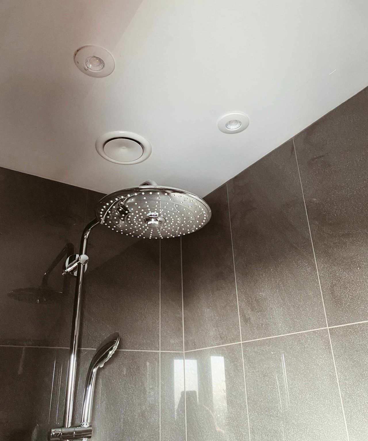Bathroom with tiled wall and large shower head showing MVHR white vent above the shower