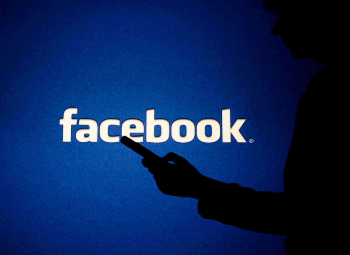 A shadowy figure using a smartphone in front of the Facebook logo