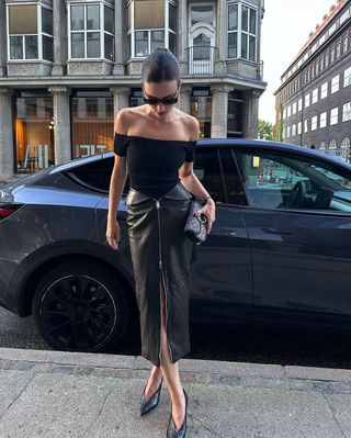 fashion influencer Lida Krasniqi wearing a black off-the-shoulder top, leather zip-up midi skirt, and black pumps