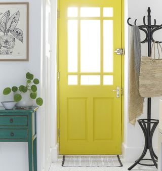 White hallway with a bright yellow front door and a coat stand for coats