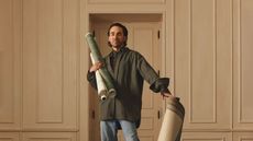 Jake Arnold posing with wallpaper and rugs from his latest collection with Lulu and Georgia