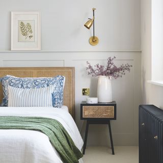 main bedroom with rattan headboard and bedside table with brass wall light and white bedlinen with green throw