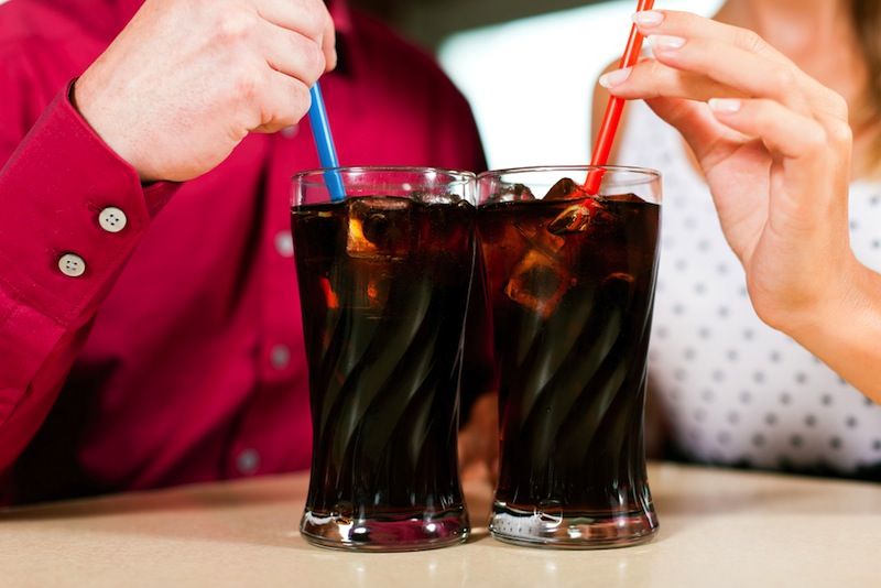 Two people drink sodas out of straws.