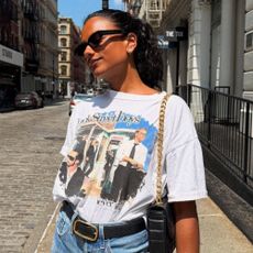 Actor Simone Ashley wears a graphic t-shirt with denim shorts, a leather bag and a black leather belt.