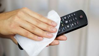 A close-up of a person's hands as they wipe down a TV remote control with a tissue