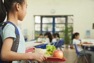 A girl takes her lunch toward a seat in a school cafeteria