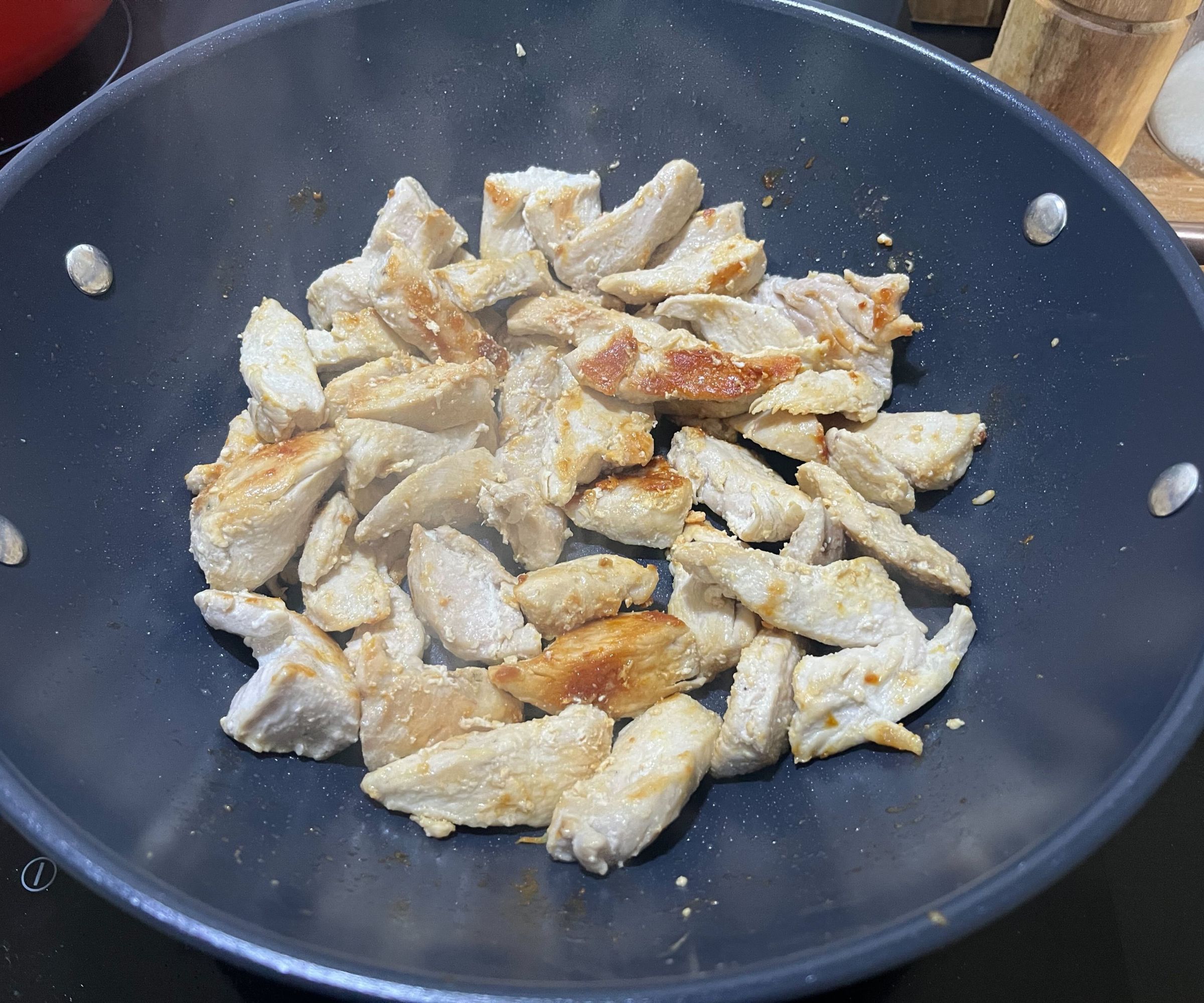 Chicken browning in a blue ceramic wok