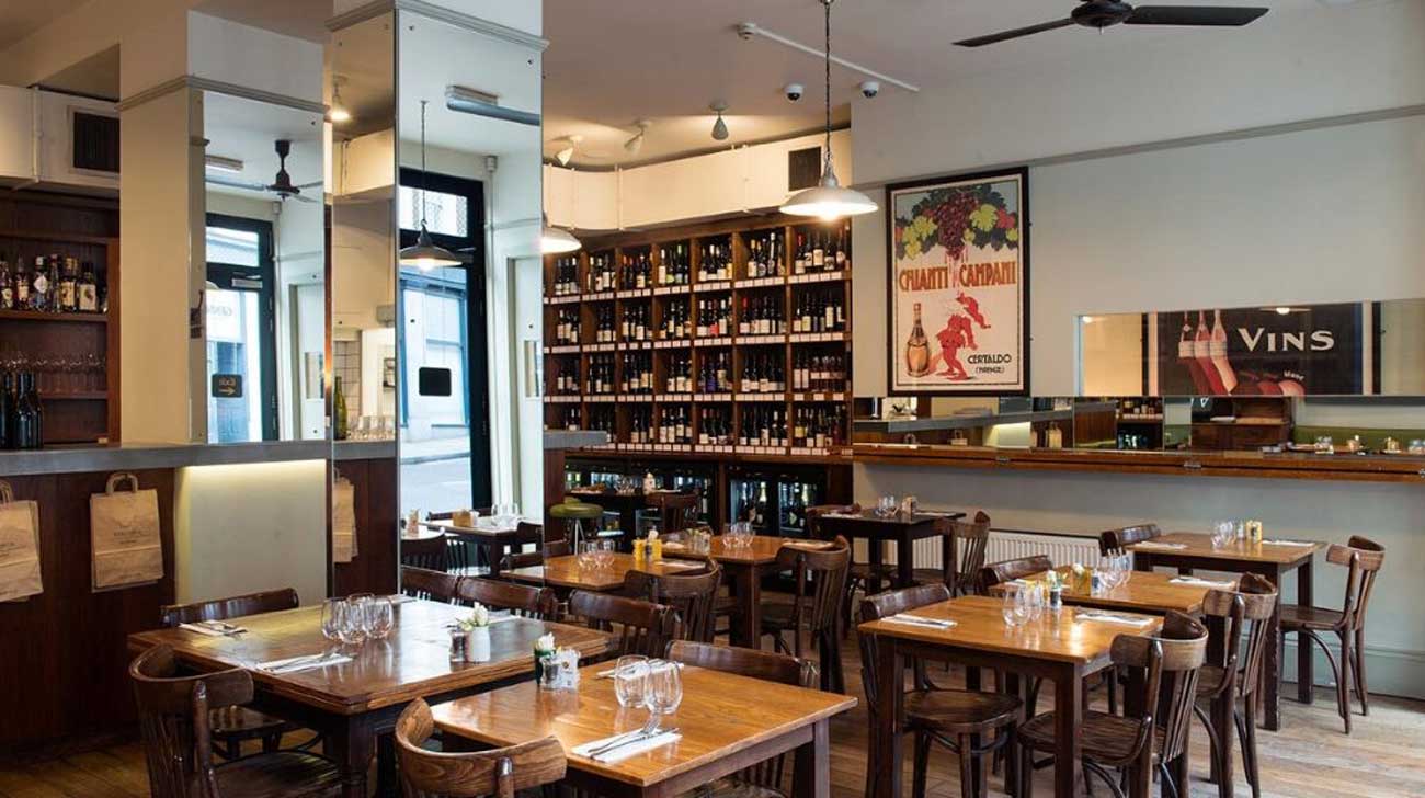 Tables and chairs inside a wine bar with shelves of wine