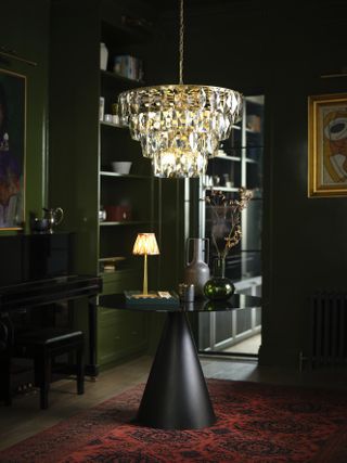 A dark green color drenched entryway with a round table and a large glass chandelier