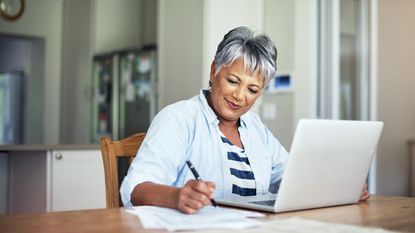 A woman looks at her spending habits on a computer with a pen and paper.