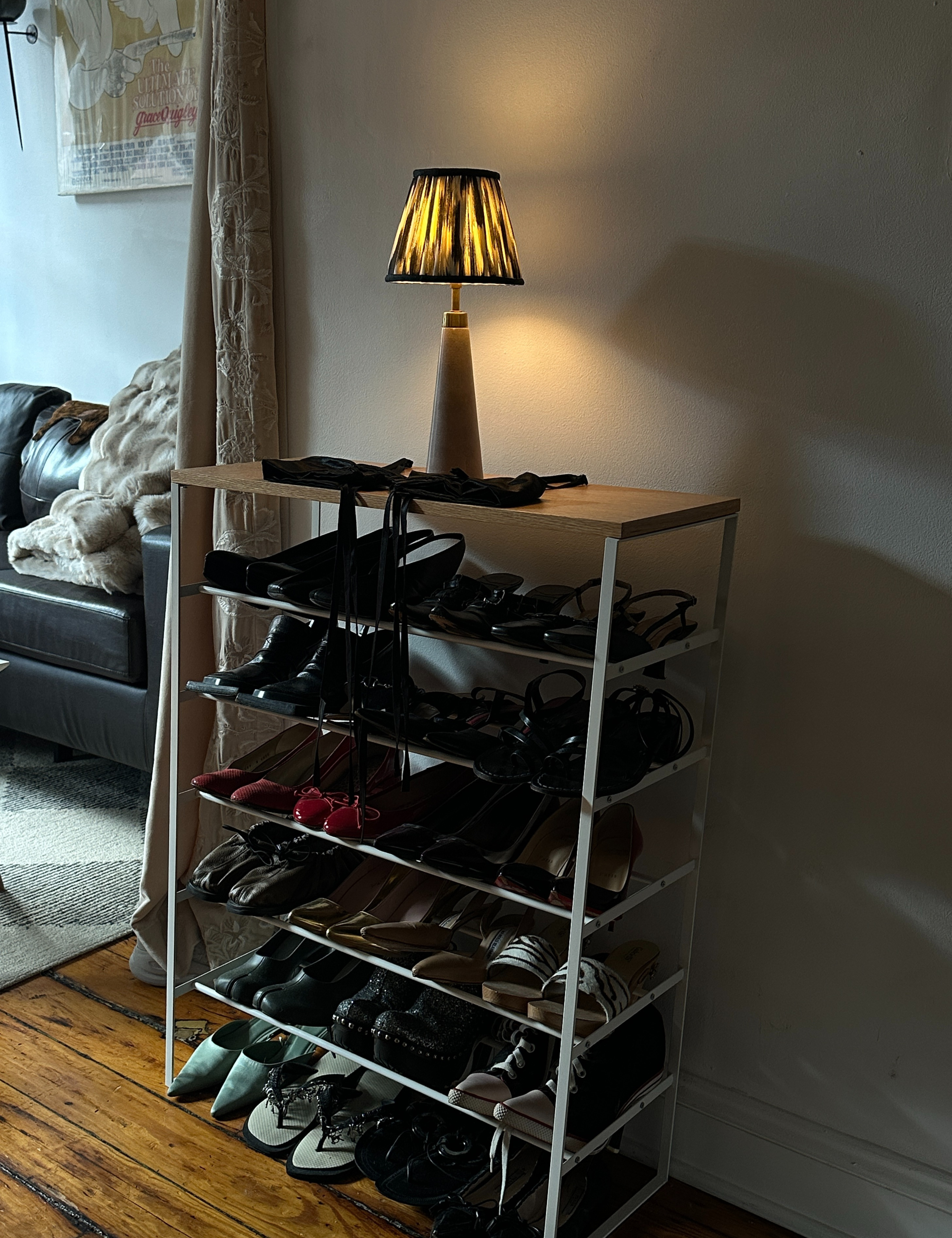 Ikat shaded Pooky table lamp resting atop of a shoe rack in a dimly lit living room