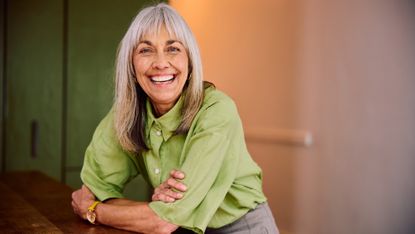 Happy mature woman smiling while leaning on table 