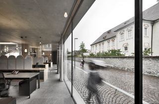 Inside office with concrete ceiling, full height glazing with view out to cobbled street on cloudy day