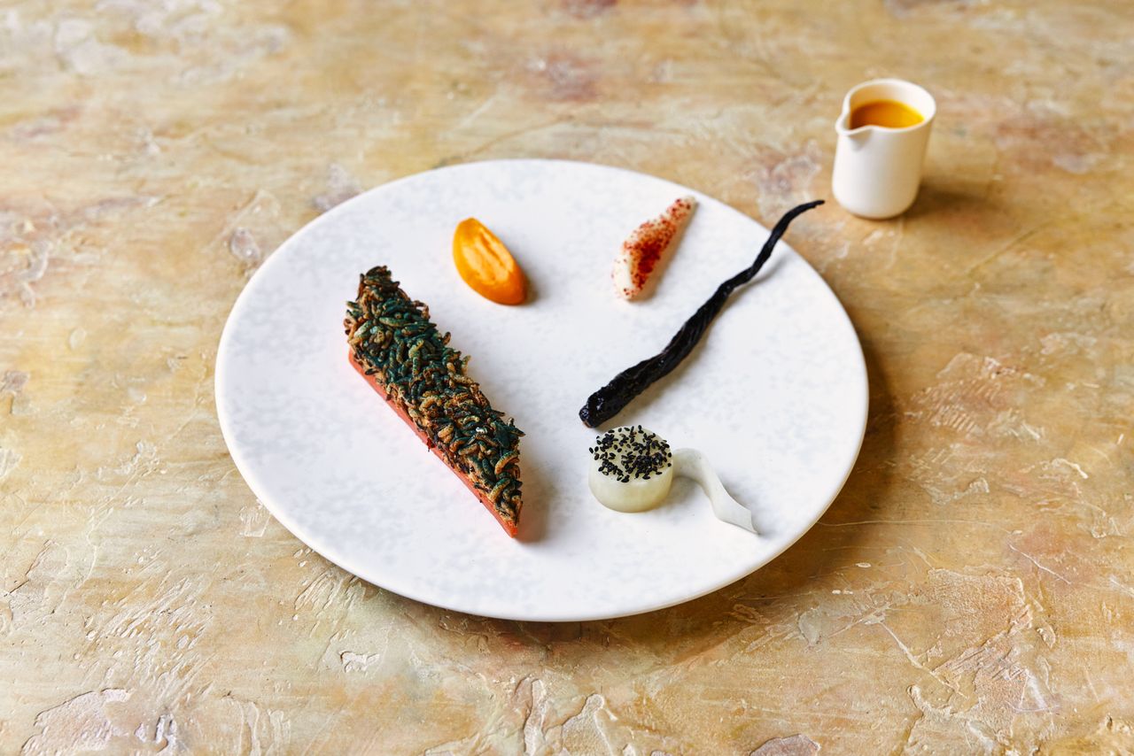 A plant-based restaurant's dishes feature greens and vegan ingredients assembled into visually striking, earthy plates served in white dishes against textural surfaces.