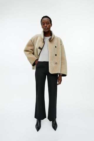 arket sale - woman wearing slightly flared black smart trousers with a shearling jacket