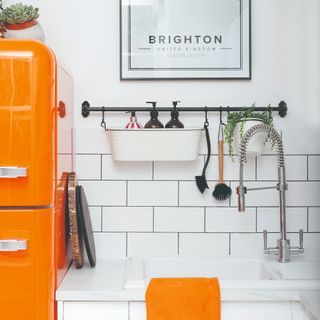 White-tiled kitchen with an orange fridge and tea towel