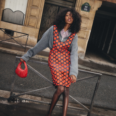 An image of an influencer wearing a Miu Miu autumn outfit featuring a red apron dress, grey jumper, and a bright red bag in Paris