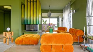 Matcha green living room with ombre irridescent yellow-green tubular fireplace, orange velvet sofas and freestanding wood sculptural floor lamp
