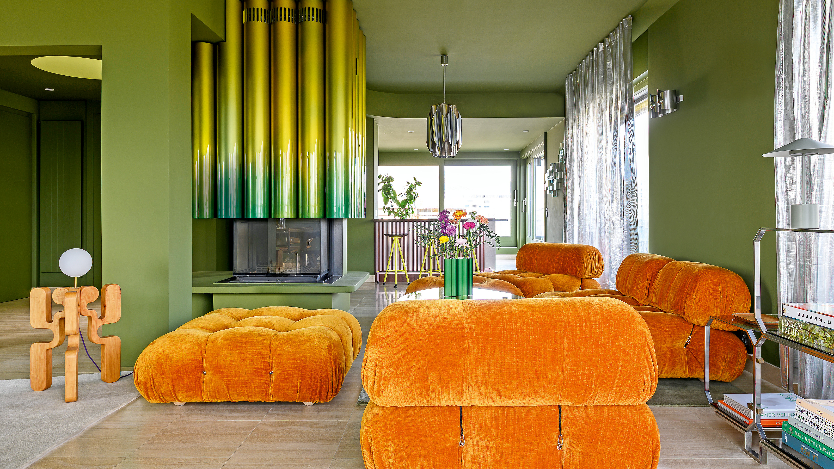Matcha green living room with ombre irridescent yellow-green tubular fireplace, orange velvet sofas and freestanding wood sculptural floor lamp