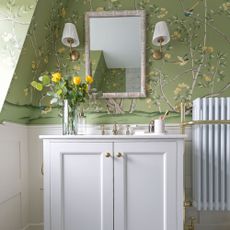 Green floral wallpaper with white vanity cabinet and bamboo mirror with wall lights