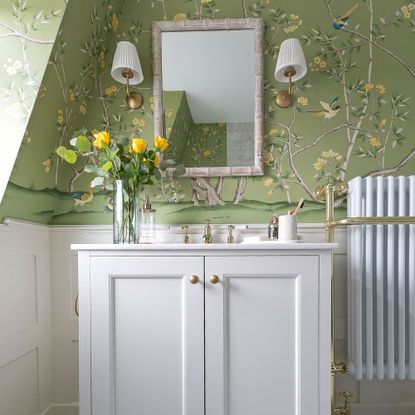 Green floral wallpaper with white vanity cabinet and bamboo mirror with wall lights