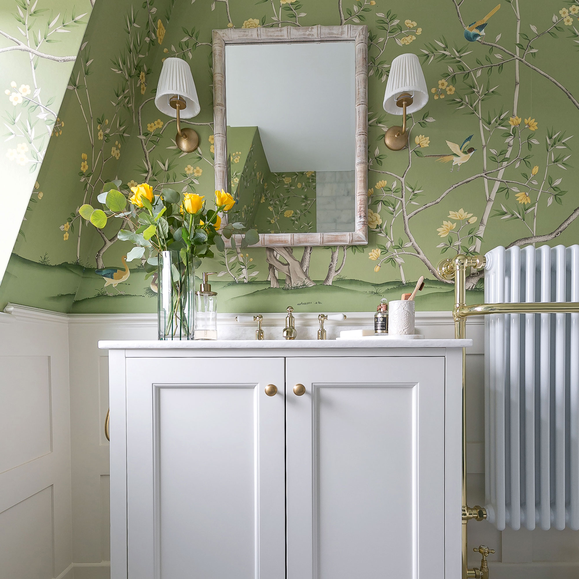 Green floral wallpaper with white vanity cabinet and bamboo mirror with wall lights