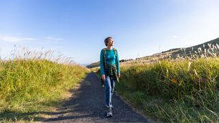 Woman walking down countryside path wearing activewear and backpack