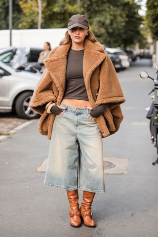 woman wearing teddy coat, t-shirt, baseball cao, denim bermuda shorts, and boots