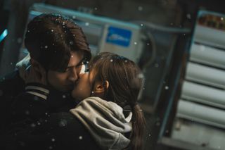 Two people (Choi Woo-shik and Park Bo-young) kiss while standing outside a phone booth in the snow.